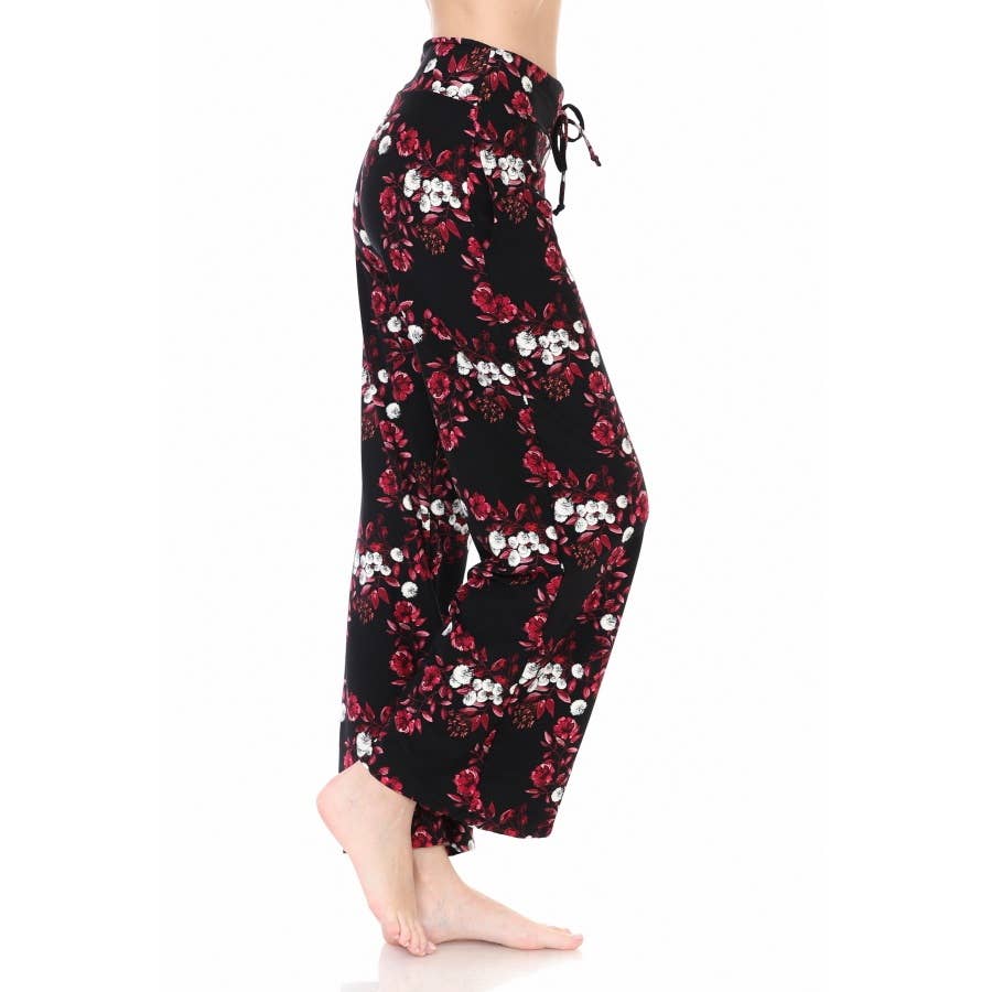 A person models Leggings Depot Buttery Soft Print Pajama Pants with a red floral and white design, high-waisted loose fit, elastic waistband, and drawstring, standing barefoot on a white background.