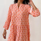 A woman in a Shewin Orange Floral Button V Neck Bell Sleeve Mini Dress stands against a plain background, smiling and gently touching her hair.