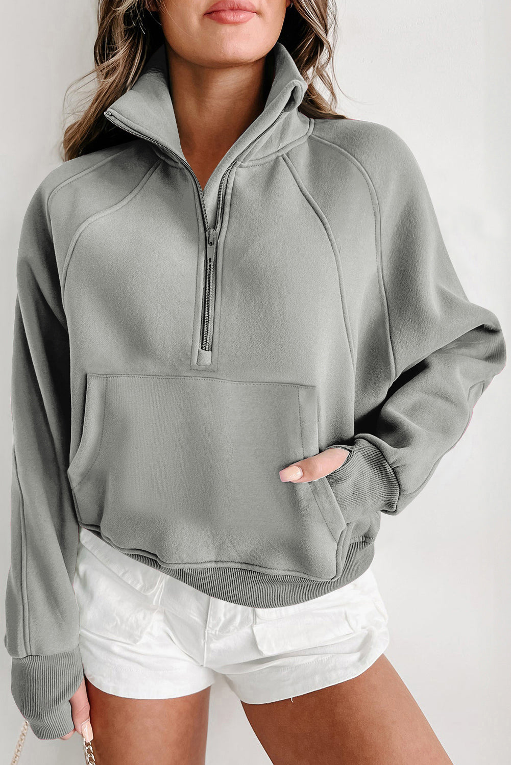 A woman with long, wavy hair wears a versatile Shewin Gray Zip Up Stand Collar Ribbed Thumbhole Sleeve Sweatshirt and white shorts, standing with her back partially turned.