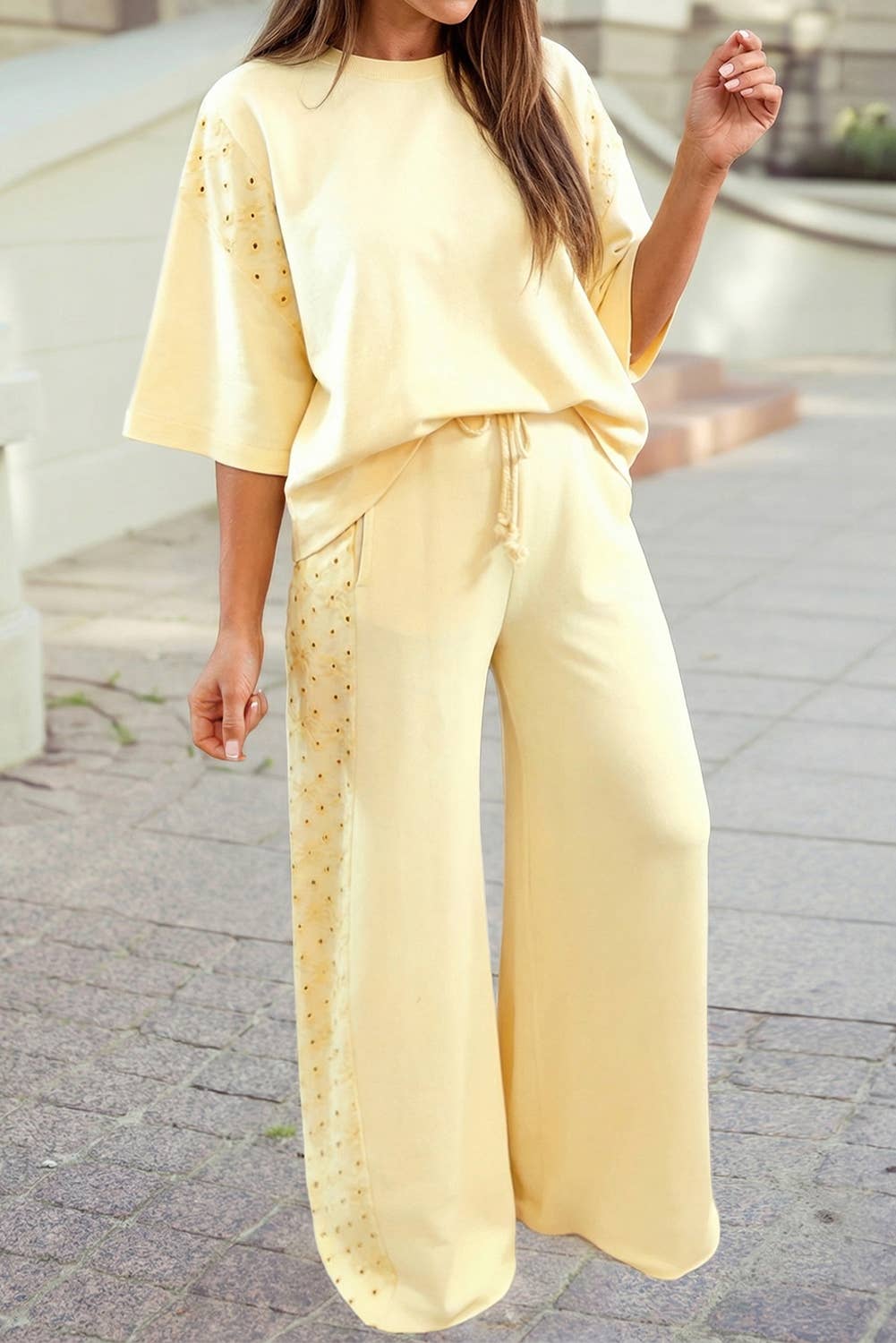 A woman walks outdoors on a paved surface wearing the 1 the Woman Oversize Tee Drawstring Loose Pants 2pcs Outfit, featuring a light yellow oversize tee and matching studded loose pants.