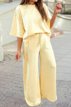 A woman walks outdoors on a paved surface wearing the 1 the Woman Oversize Tee Drawstring Loose Pants 2pcs Outfit, featuring a light yellow oversize tee and matching studded loose pants.