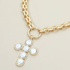 Sensibling Corp.’s Pearl Cross Charm Pendant Chunky Chain Statement Necklace features a textured gold chain with a round clasp and a striking cross pendant crafted from five circular white pearls set in gold.