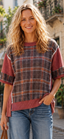 A woman with wavy blonde hair smiles at the camera while standing outdoors, wearing blue jeans and the Celeste Clothing Plaid Contrast Trim Rib Knit Oversized Short Sleeve Top.