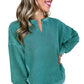 A smiling person poses with one hand on their hip, wearing a Notched Neck Exposed Seam Drop Shoulder Sweatshirt in green by Shewin and white pants.