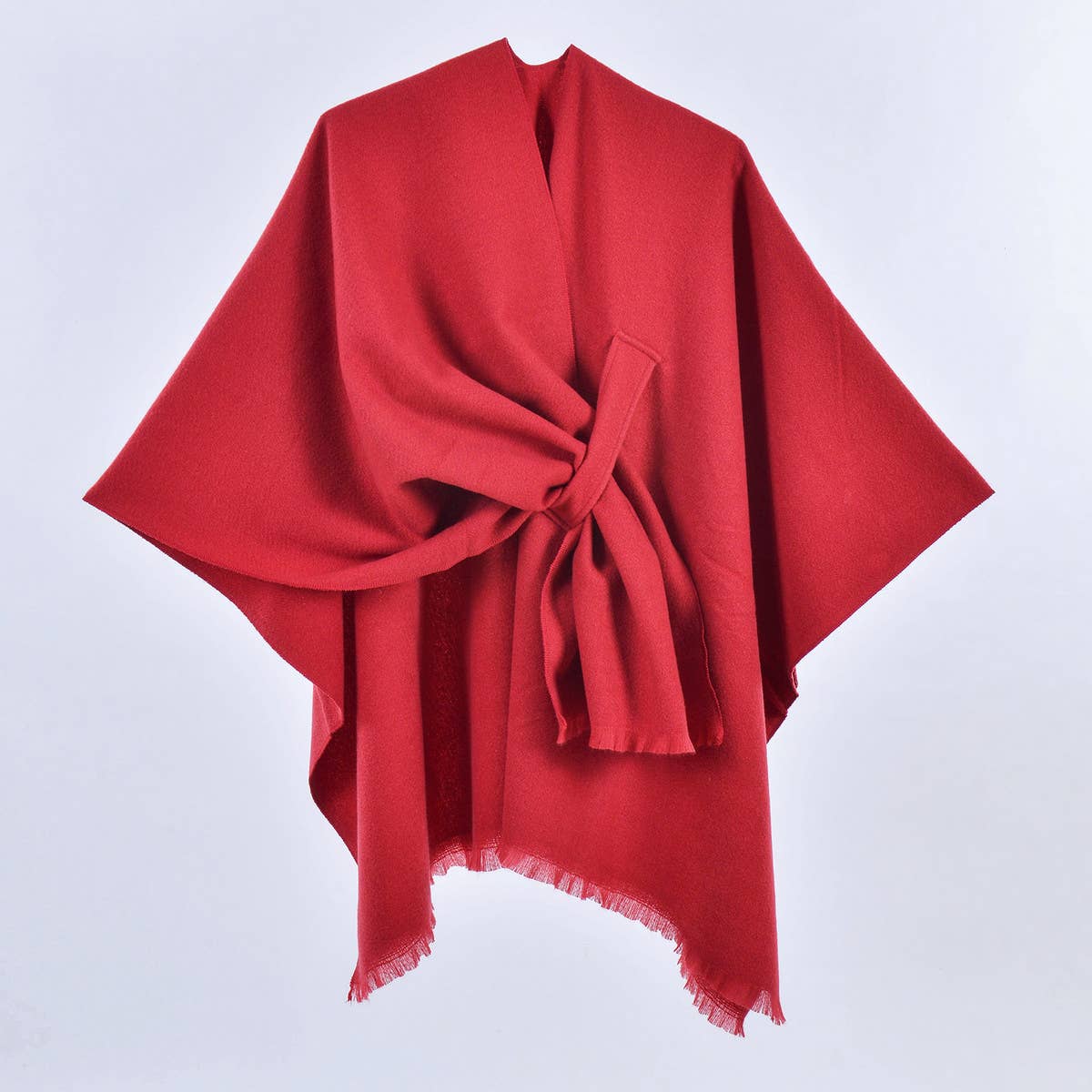 The ACCITY SIMPLE SOLID COLOR OBLIQUE STRAP CAPE SHAWL, shown in red with a knotted front and fringed edges against a white background, is the ideal layering piece for any outfit.