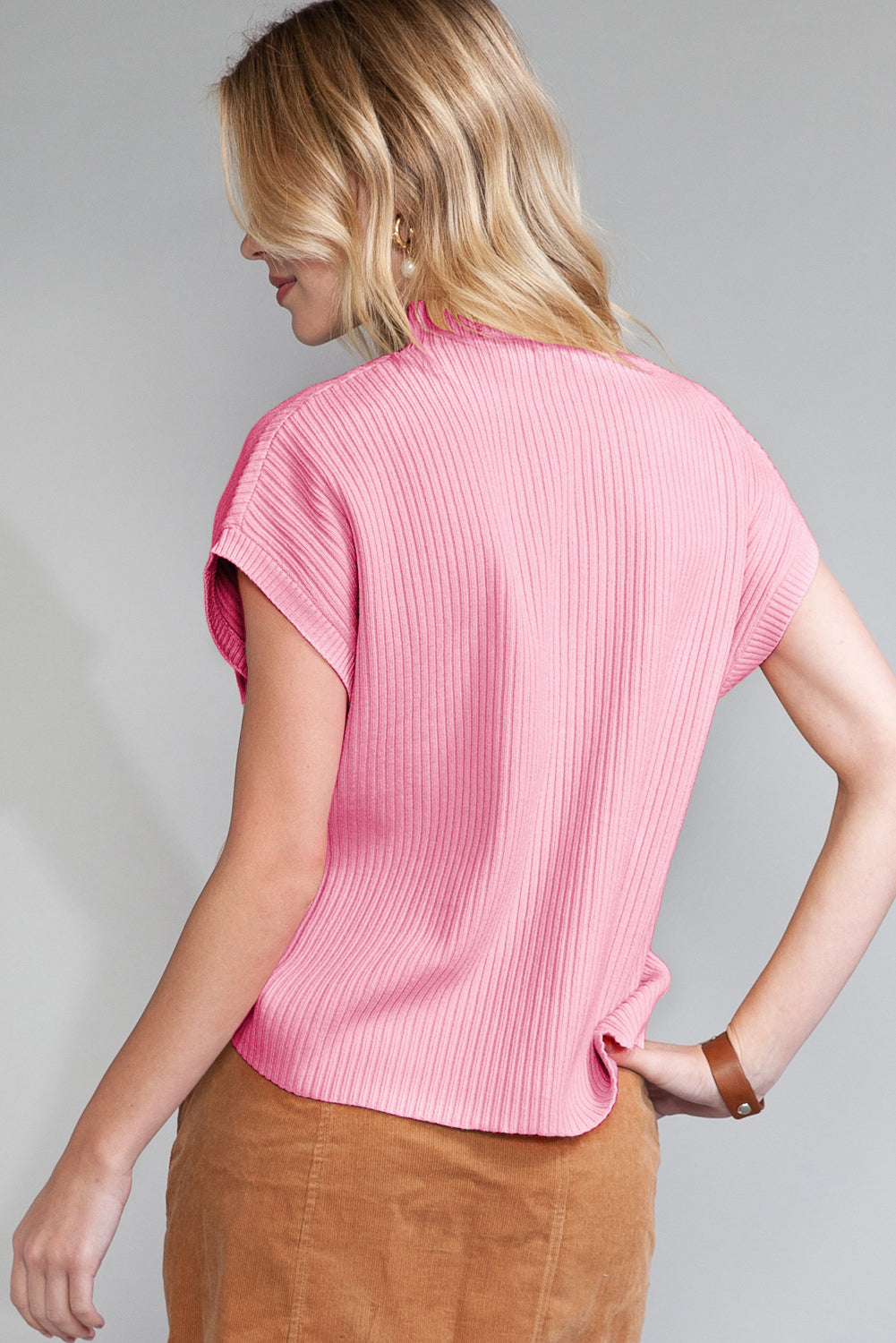 A blonde woman faces away, wearing Shewin's Patch Pocket Ribbed Knit Short Sleeve Sweater in pink paired with a brown skirt, ideal for transitional weather.