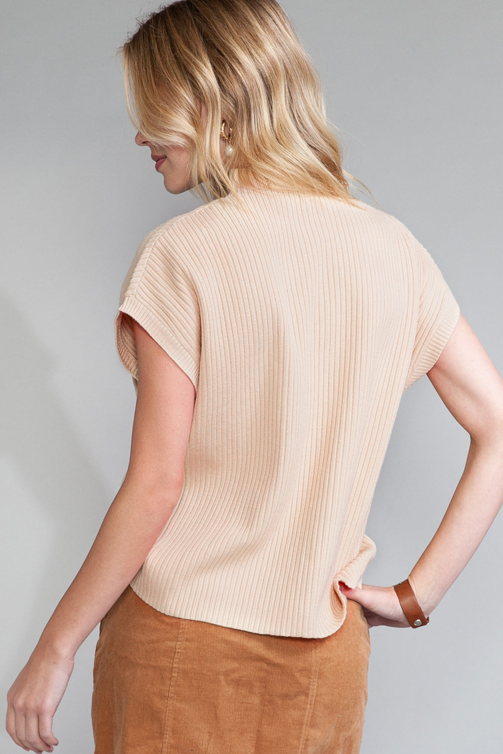 Seen from behind, an individual wears a beige Shewin Patch Pocket Ribbed Knit Short Sleeve Sweater paired with a brown skirt, demonstrating a stylish and comfortable ensemble perfect for transitional weather.