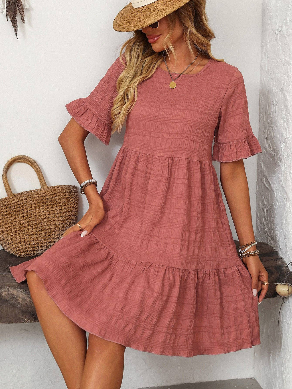 A woman in the Suhkasana Loose Casual Short-Sleeve Dress and straw hat sits indoors with a straw handbag, embodying effortless summer style.