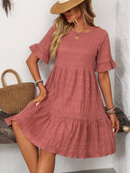 A woman in the Suhkasana Loose Casual Short-Sleeve Dress and straw hat sits indoors with a straw handbag, embodying effortless summer style.