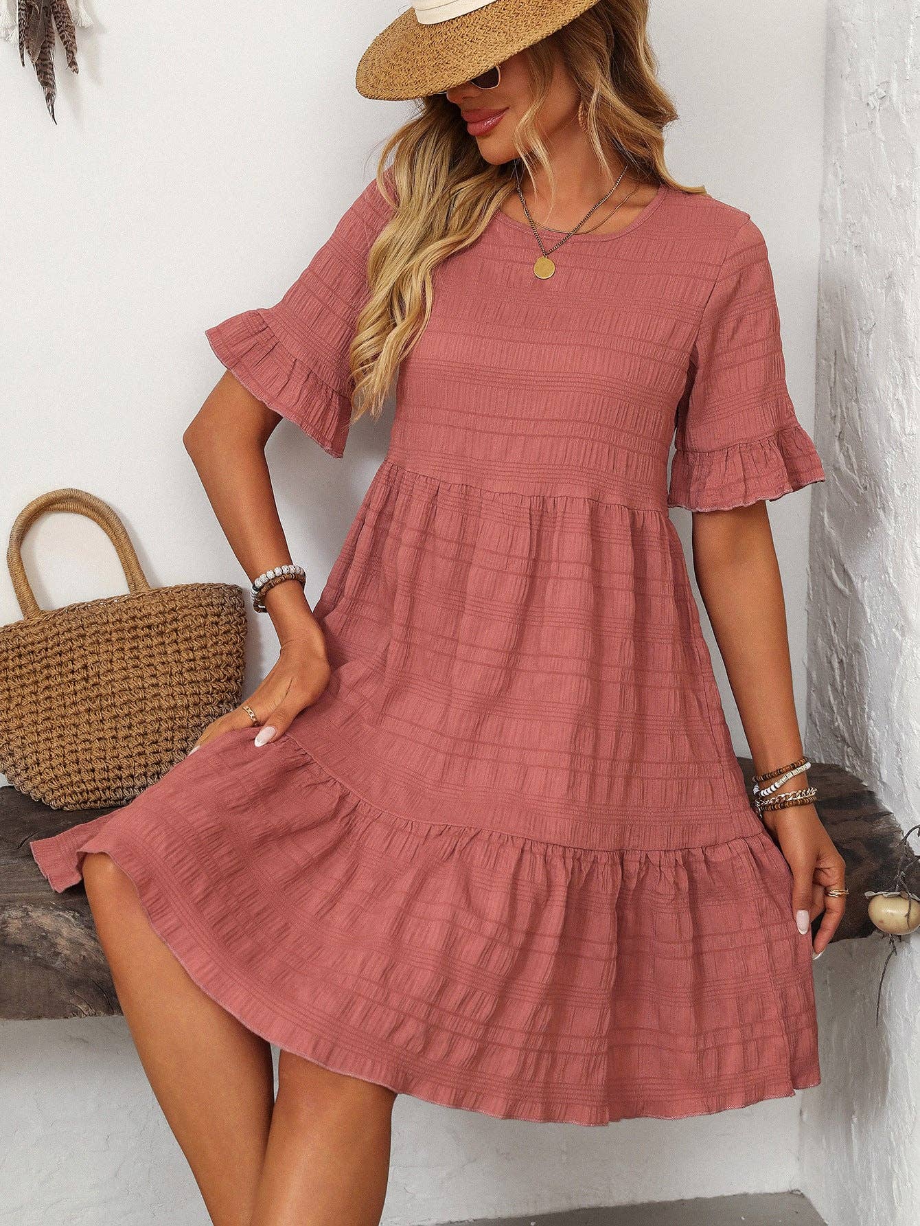A woman in the Suhkasana Loose Casual Short-Sleeve Dress and straw hat sits indoors with a straw handbag, embodying effortless summer style.