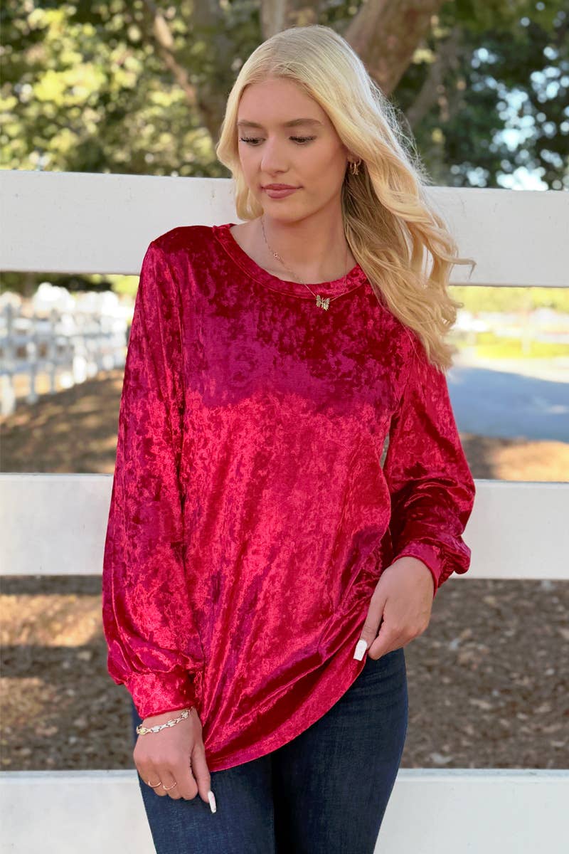 A woman with long blonde hair wears the 24-Hrs Fashion Crushed Velvet Top in bright pink with flowy sleeves and dark jeans, standing by a white fence with trees behind her.