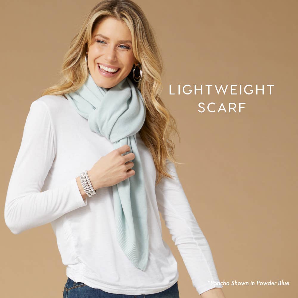 A woman in a white long-sleeve shirt and light blue Lightweight Ponchos Wrap by COCO + CARMEN smiles against a beige background. Caption reads "Lightweight Ponchos Wrap"—perfect for layering or pairing with your favorite scarf.
