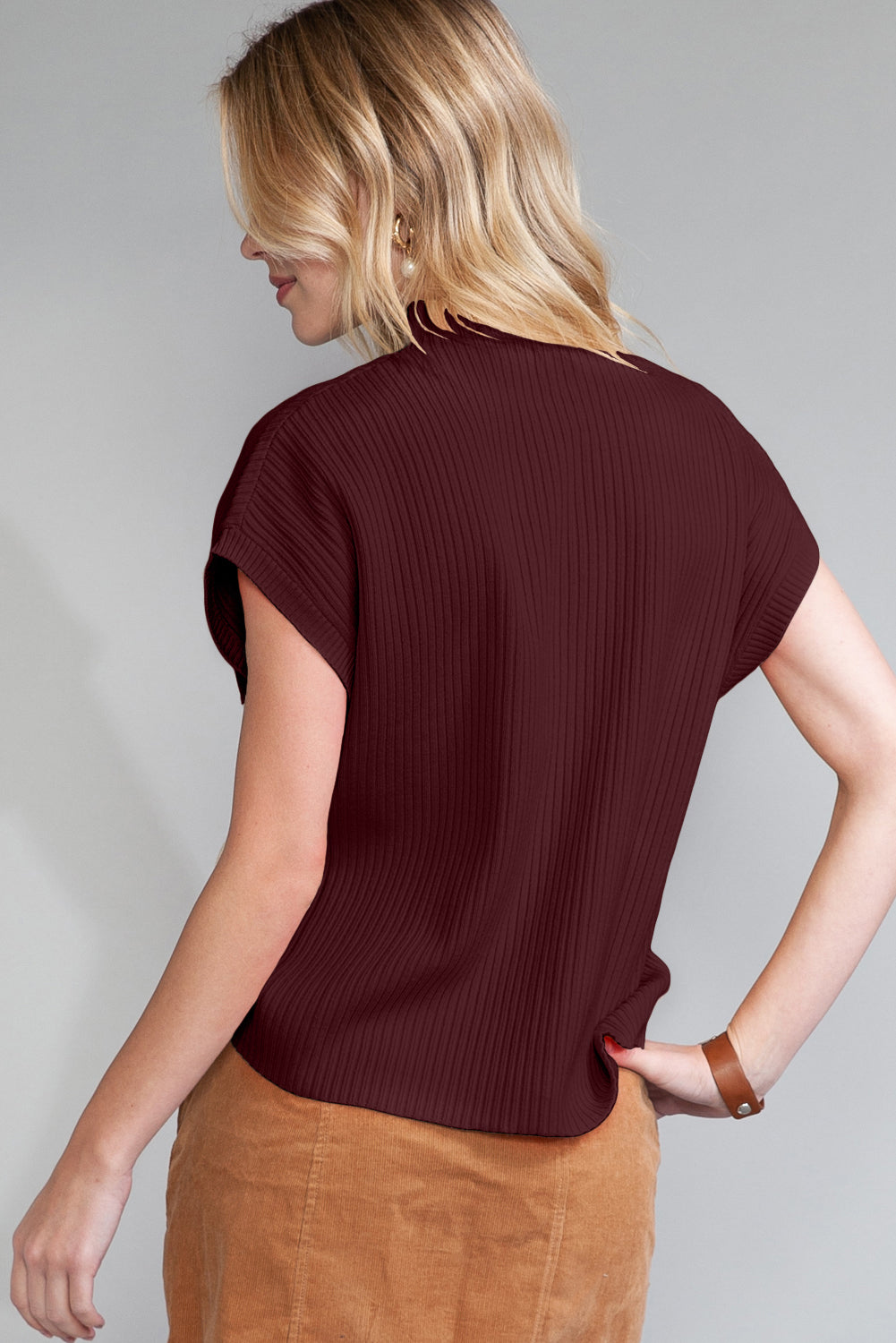 A person with blonde hair is wearing the maroon Shewin Patch Pocket Ribbed Knit Short Sleeve Sweater and brown pants, viewed from the back against a gray background. This stylish and comfortable outfit is perfect for transitional weather.