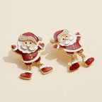 The Enamel Glitter Santa Dangle Earrings from Lilla Haven feature a festive Santa Claus design with red and white enamel, gold outlining, and pearl accents. Displayed on a beige background, these Pearl Holiday Statement Earrings are the perfect accessory to brighten up your seasonal look.