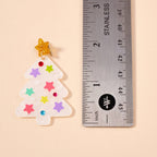The Glittery Christmas Tree Drop Earrings by Lilla Haven, featuring a festive tree shape adorned with colorful stars reminiscent of holiday ornaments, are displayed next to a stainless steel ruler for scale, showing each acrylic earring measures approximately 2 inches tall.
