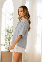 A woman poses indoors in the Sew In Love Relaxed Fit Collared V Notch Neck Striped Top, her wavy hair framing a neutral expression as sunlight streams through arched windows behind her.