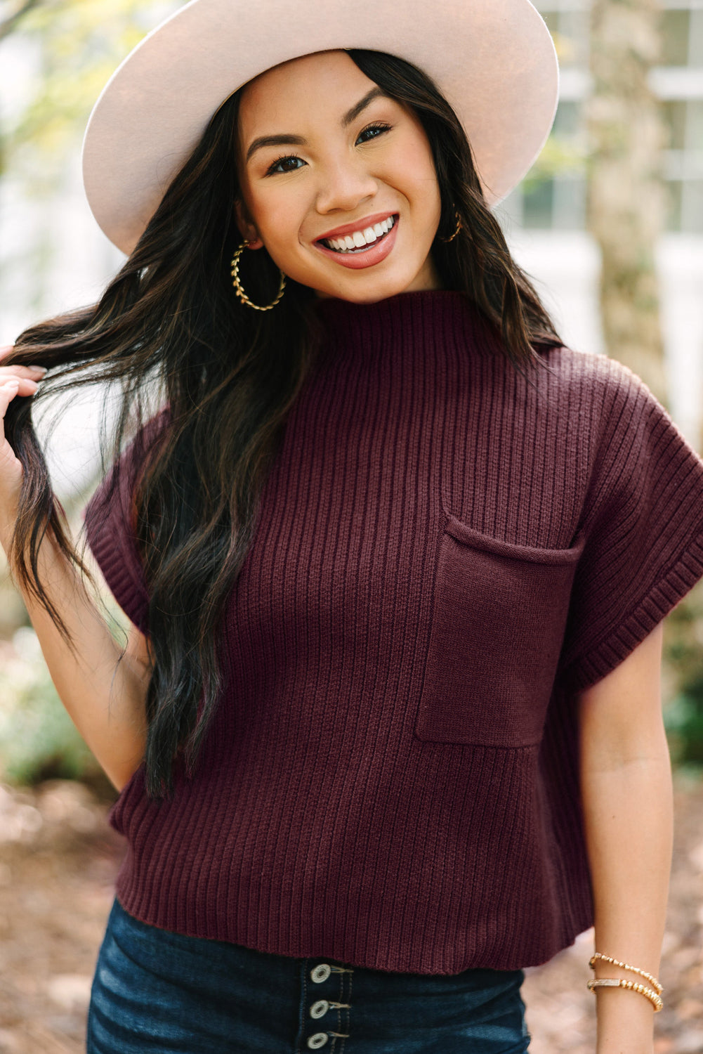 A person embraces the casual style of transitional weather, smiling at the camera while wearing a wide-brimmed hat and a Shewin Patch Pocket Ribbed Knit Short Sleeve Sweater, standing outdoors with trees in the background.