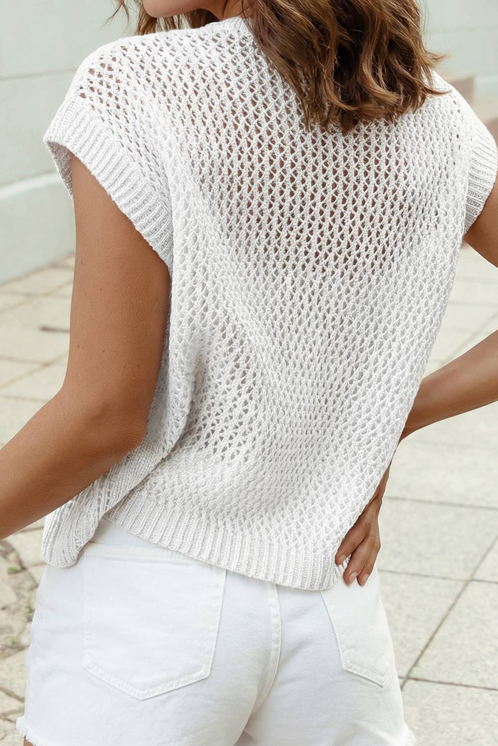 A person wearing the 1 the Woman Flag Graphic Short Sleeve Sweater Top and white shorts stands outdoors with their back to the camera.