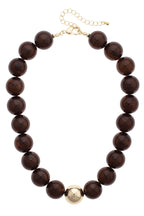 The Marjorie Fall Beaded Necklace by Canvas Style features oversized dark brown resin beads, a single central gold bead, and is finished with a gold chain extender and clasp.