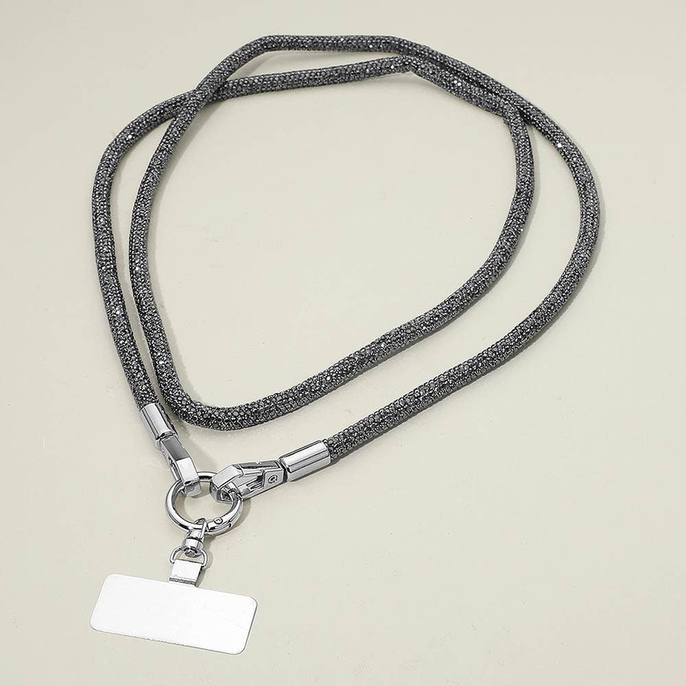 A Sensibling Corp. Rhinestone Phone Lanyard Necklace featuring metallic clasps and a blank rectangular identification badge is displayed on a light-colored surface.