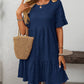 A woman in a Suhkasana Loose Casual Short-Sleeve Dress, paired with a woven straw handbag, sunglasses, bracelets, necklaces, and a hat—a chic look for stylish summer days.