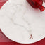 Seasons Jewelry's Alabama Glitter Enamel Logo Necklace, featuring a silver chain with round beads and a crimson “A” logo pendant in glitter enamel, is displayed on a round white marble surface beside a red glass bottle.