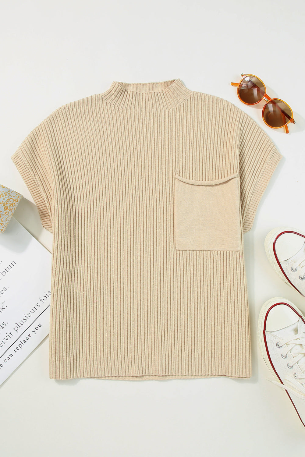 The Shewin Patch Pocket Ribbed Knit Short Sleeve Sweater, ideal for transitional weather, is shown laid flat with sunglasses, white sneakers, and patterned fabric.