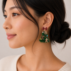 A woman with dark hair in a low bun wears Lilla Haven’s Tinsel Christmas Tree Drop Earrings, featuring holiday ornament charms, a red bow, and a gingerbread man. Styled with a light-colored sweater, her look is the perfect choice for anyone who loves playful festive jewelry.