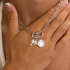 A hand holds the WJW 18K Gold PVD Paperclip Carabiner Necklace, adorned with three charms—a tennis racket, the letter "A," and a white four-petal flower—highlighting this stylish, customizable piece perfect for personal expression.