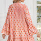 A woman is wearing the Shewin Orange Floral Button V Neck Bell Sleeve Mini Dress in a bright room with large windows.