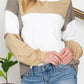 A woman wearing the Shewin Khaki Color Block Exposed Seam Long Sleeve Top paired with blue jeans, standing indoors with a plant and picture frame in the background.