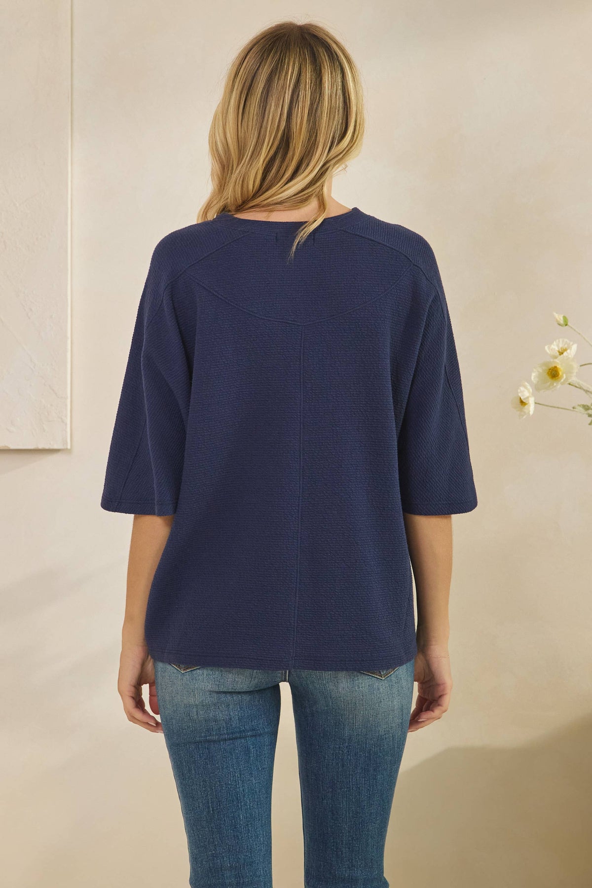 Back view of a person wearing a navy blue, textured CLOUDY KNIT 3/4 SLEEVE ROUND NECK TOP paired with blue jeans.