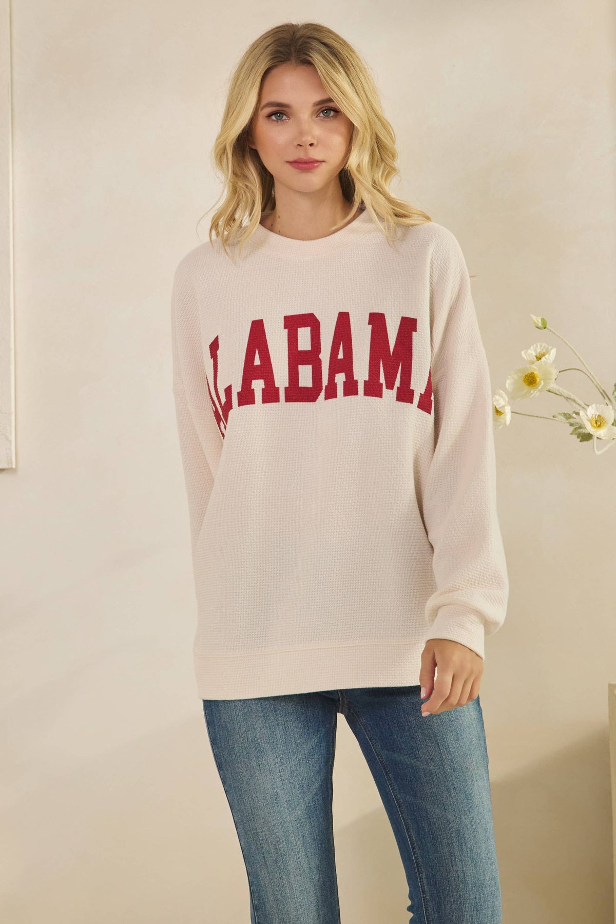 A person wears a beige long-sleeve ALABAMA Cloudy Soft Knit Long Sleeve Top with “ALABAMA” in red collegiate lettering across the chest.