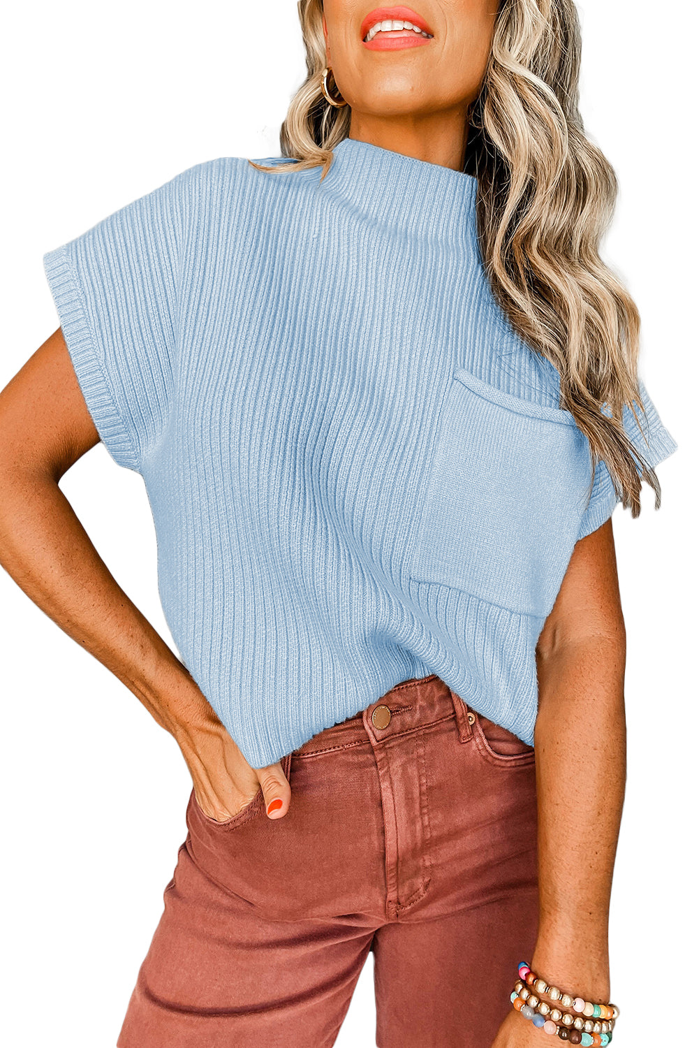 A person models Shewin's Patch Pocket Ribbed Knit Short Sleeve Sweater in light blue with brown pants on a white background, showcasing an ideal ensemble for transitional weather.