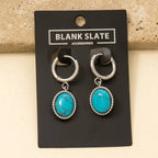 Anarchy Street's Oval Turquoise Stone Drop Earrings feature silver hoops and turquoise pendants, displayed on a black card. Made of stainless steel, these earrings add an elegant touch to any outfit.