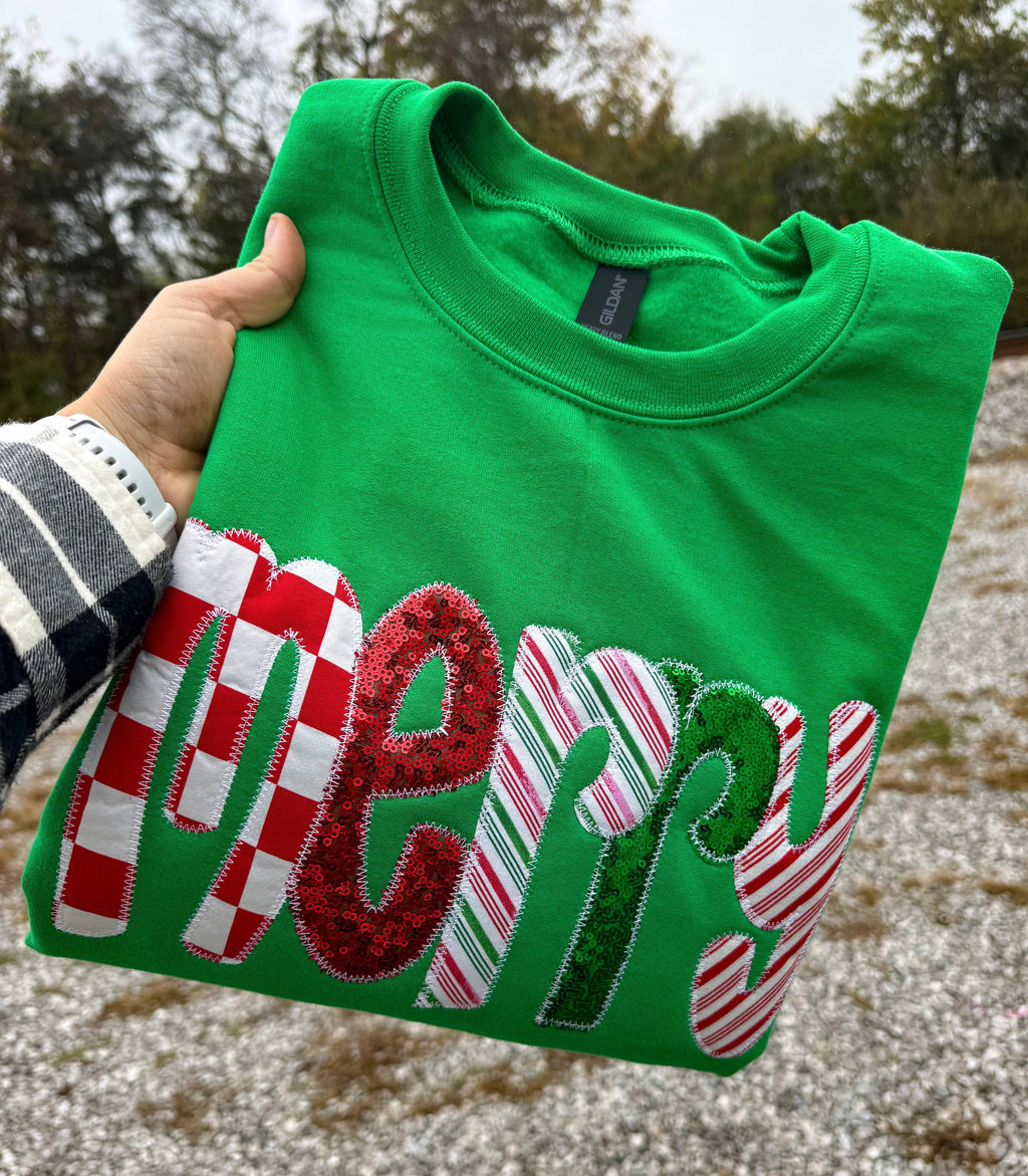 Faire Green Merry Sequin Christmas Sweatshirt in bright green with “Merry” appliqued on the front in red, white, and green candy cane-patterned and sequined fabric.