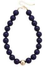 The Marjorie Game Day Beaded Necklace by Canvas Style features large, round dark oversized beads accented with a central gold bead, finished with a gold clasp and adjustable chain—making it the perfect bold statement necklace.
