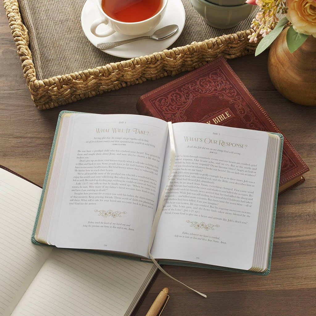 Open teal Devotional Be Still and Know Faux Leather Teal book resting on a woven tray next to a coffee cup.