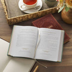 Open teal Devotional Be Still and Know Faux Leather Teal book resting on a woven tray next to a coffee cup.