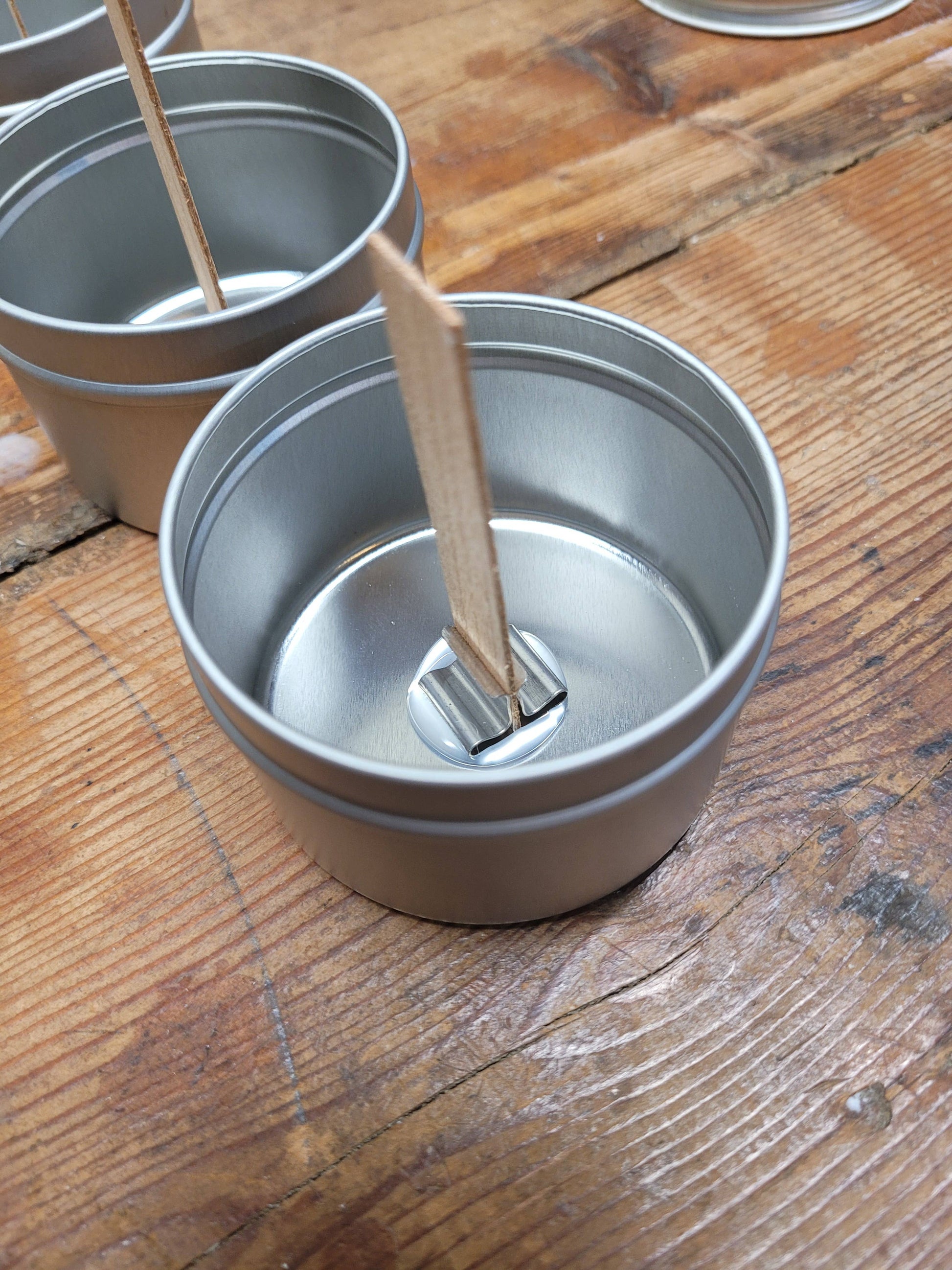 Stephanie Henry Candle Company's 4oz Handpoured Soy Wax Candles in Mahogany Teakwood are elegantly placed on a rustic wooden surface, featuring empty metal tins and wooden wicks ideal for candle crafting.