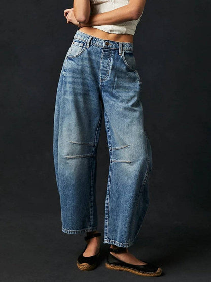 A person in Dipped Shop's Washed Mid Rise Loose Barrel Jeans, paired with a white cropped top and black espadrilles, stands against a dark background.