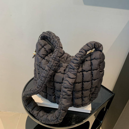 The ACCITY Puffy Cloud Bag Large Shoulder Crossbody, black and quilted with a thick padded strap, rests on a small glossy black table against a light-colored wall.