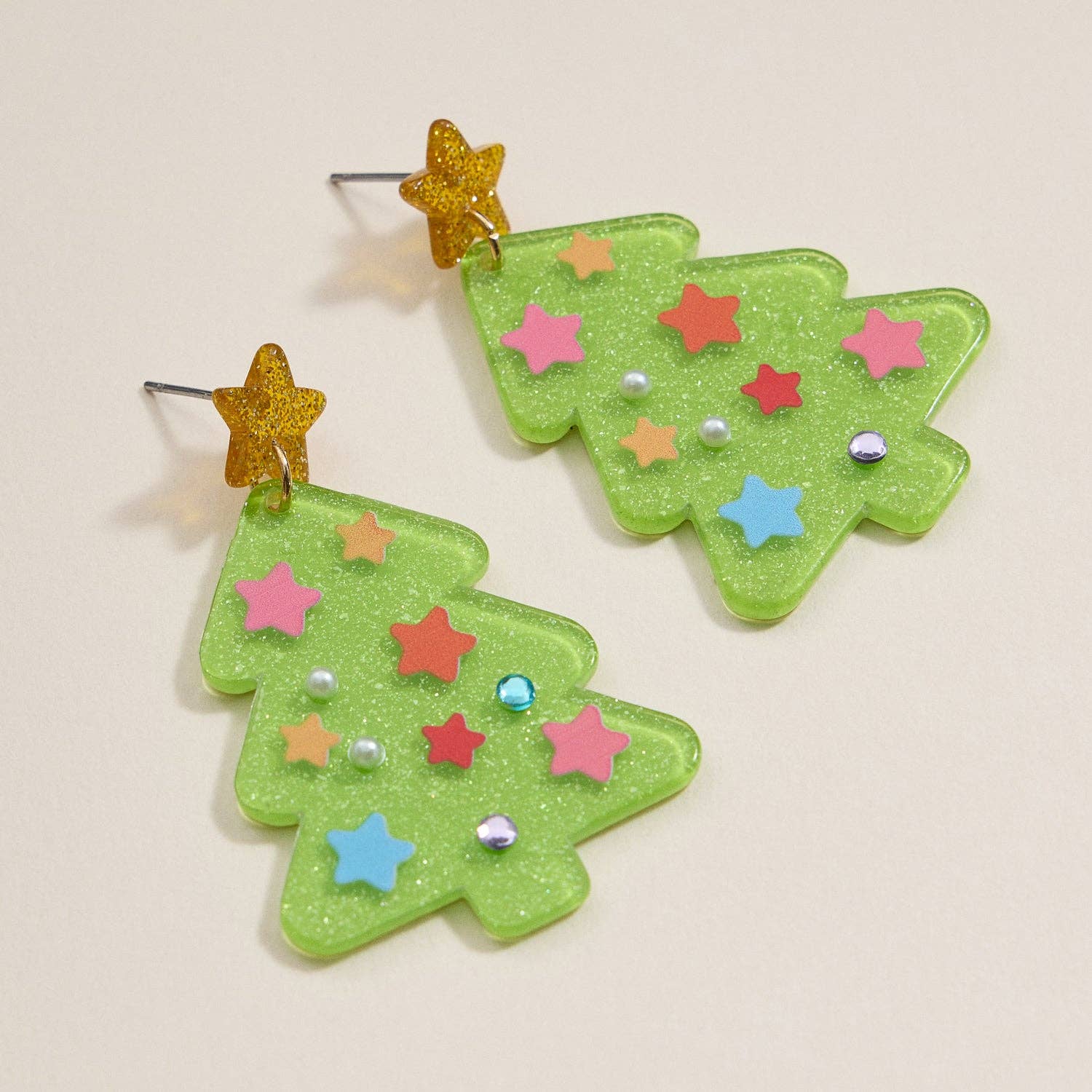 Add a festive sparkle to your holiday look with the Glittery Christmas Tree Drop Earrings from Lilla Haven. These green acrylic earrings are crafted in the shape of Christmas trees, adorned with vibrant star and gem decorations, and each is finished with a cheerful yellow star at the top. Displayed on a simple background, these eye-catching Holiday Acrylic Earrings make the perfect seasonal statement jewelry for adding charm to your festive style.