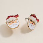 Two Santa Claus Stud Earrings from Lilla Haven, featuring red rhinestones and festive enamel detailing, are displayed on a light beige surface—making them the perfect holiday jewelry accent for any Christmas outfit.