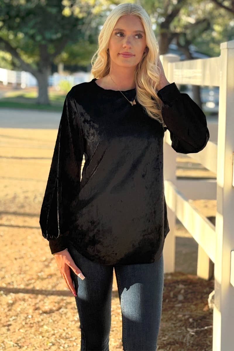 A woman with long blonde hair stands outdoors by a white fence, wearing the 24-Hrs Fashion Crushed Velvet Top and blue jeans, with trees and sunlight in the background.