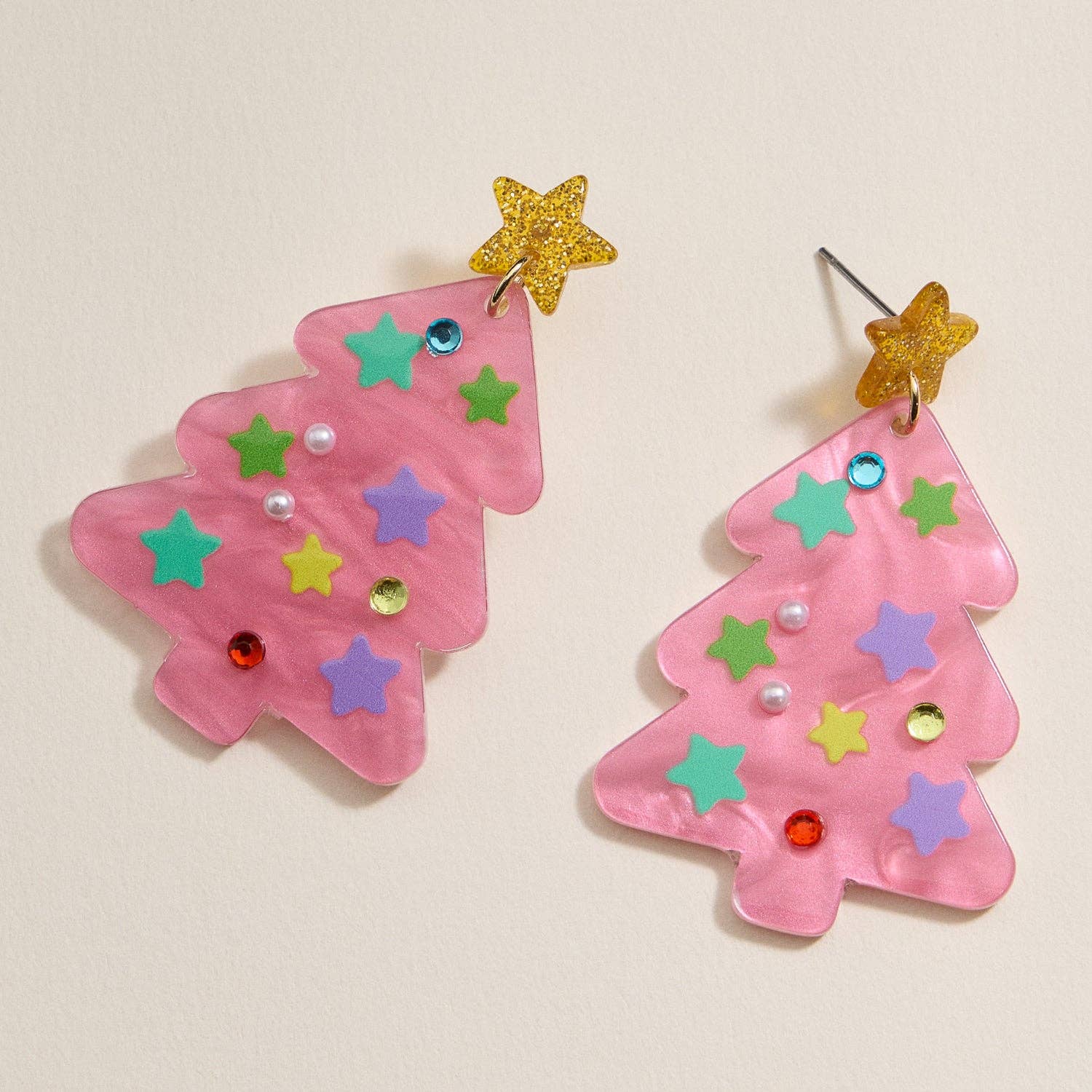 Two Glittery Christmas Tree Drop Earrings from Lilla Haven, featuring pink acrylic trees adorned with colorful stars, pearls, and rhinestones and topped with sparkling yellow stars, are displayed on a light beige background—perfect festive statement jewelry to add holiday sparkle to your look.