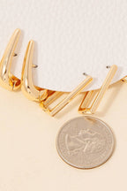 Three Mixed Long Oval Hinge Hoop Earrings by Anarchy Street and a U.S. quarter are displayed on a light surface next to textured white material.