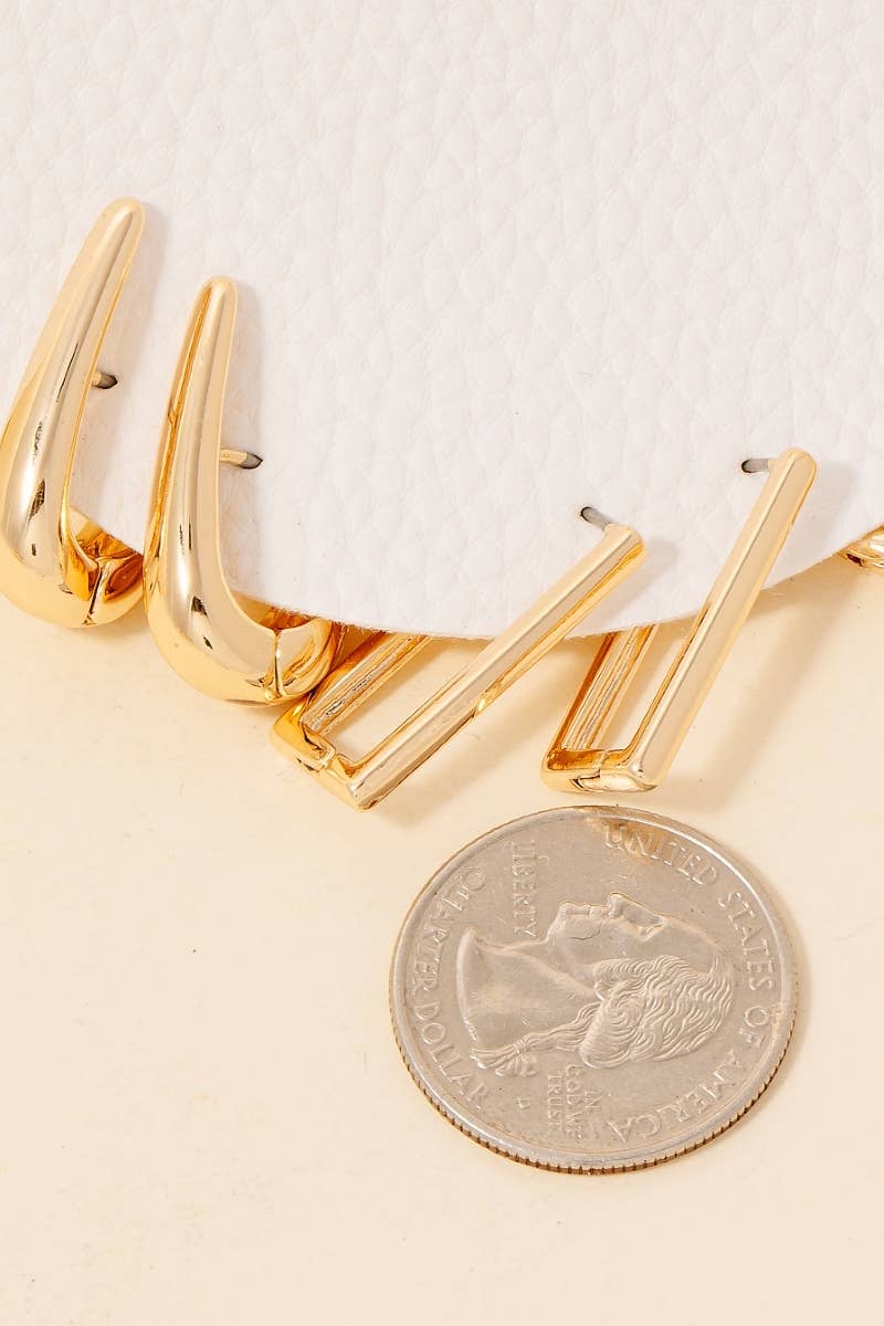 Three Mixed Long Oval Hinge Hoop Earrings by Anarchy Street and a U.S. quarter are displayed on a light surface next to textured white material.