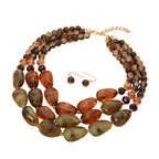 Introducing the Chunky Beaded Layered Statement Necklace by Sensibling Corp.—a striking jewelry set with three layers of oversized brown and green stones, complemented by matching round brown bead drop earrings with gold hooks.
