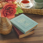 A teal Devotional Be Still and Know Faux Leather Teal resting on top of a dark brown faux leather book.